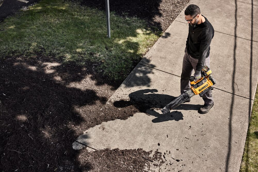 DEWALT 60V* Blower being used to blow mulch on a sidewalk by a man viewed from above. 