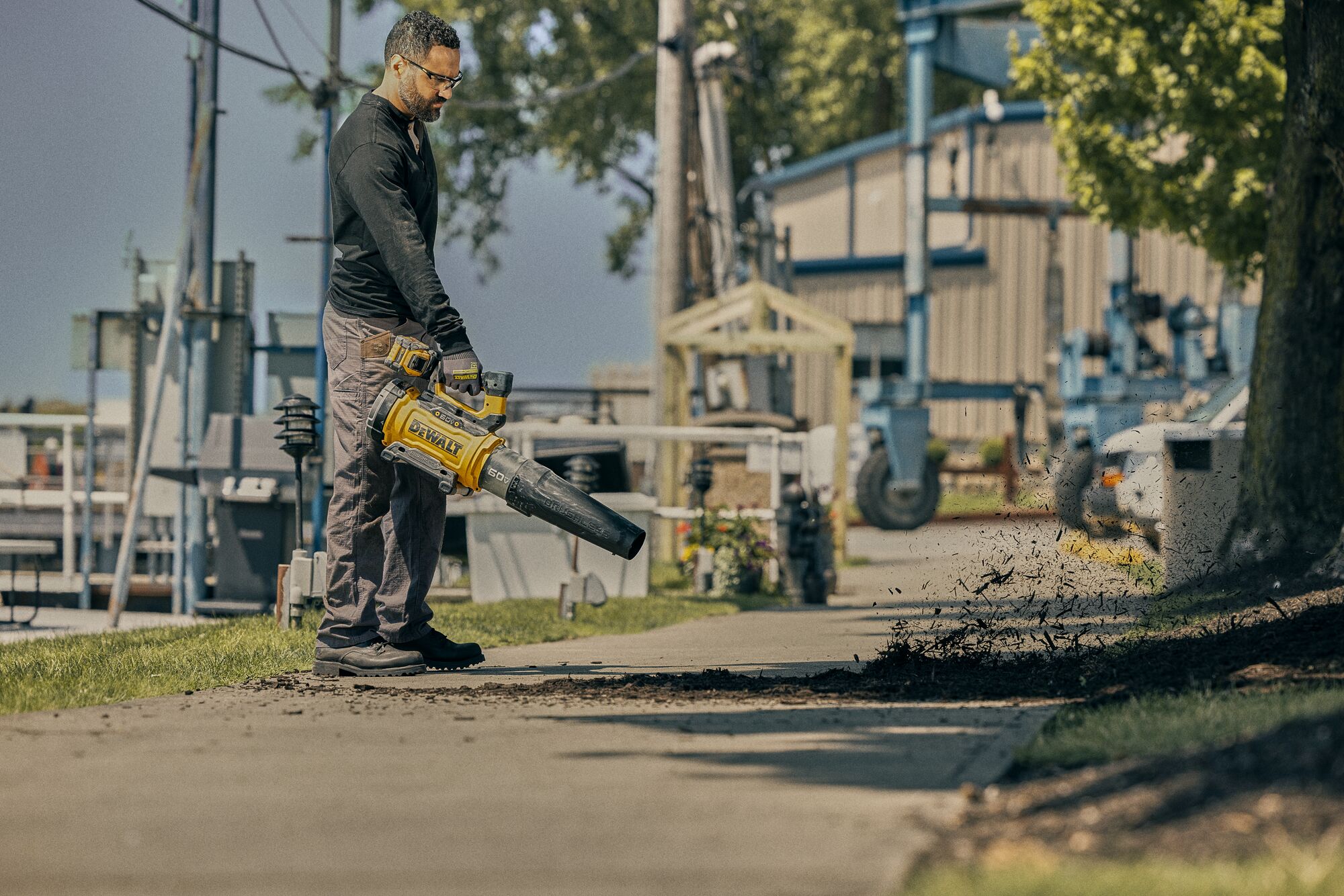 DEWALT 60V Blower being used to blow mulch by a man at an industrial location.