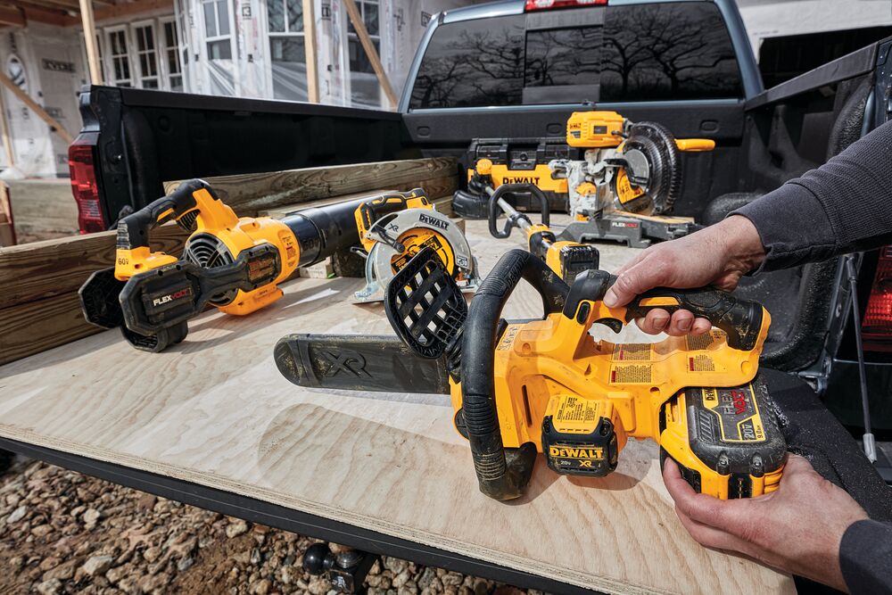 XR® Compact 12 inch Cordless Chainsaw sitting in  cargo bed of a truck with or tools, being held by a person for battery insertion