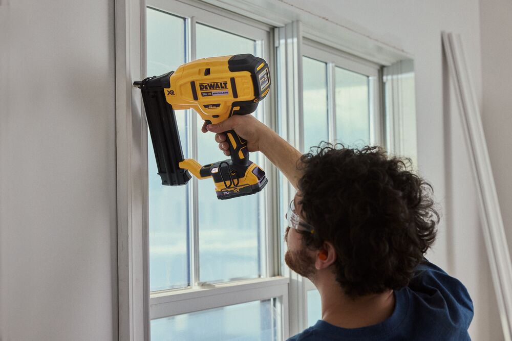 A carpenter uses a nailer on a window frame