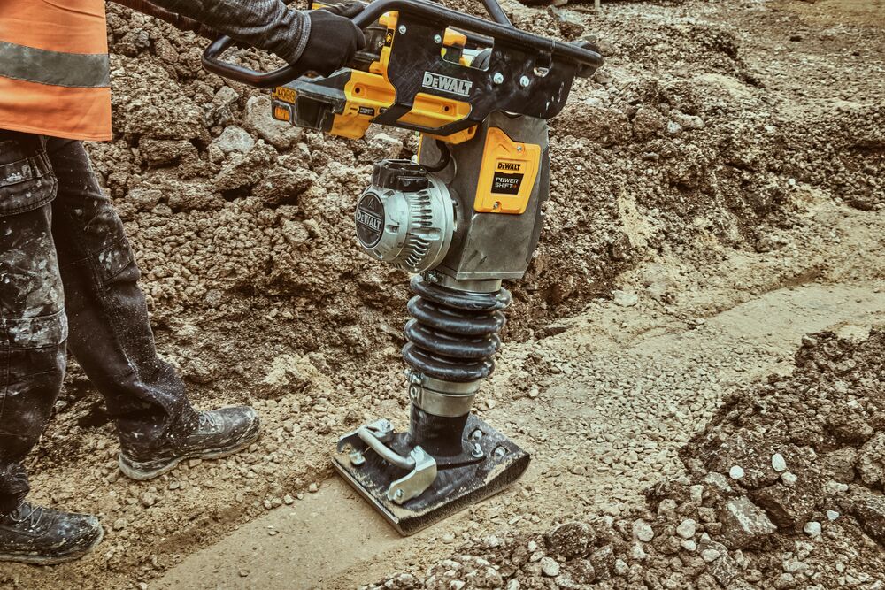 Man operating rammer in dirt trench
