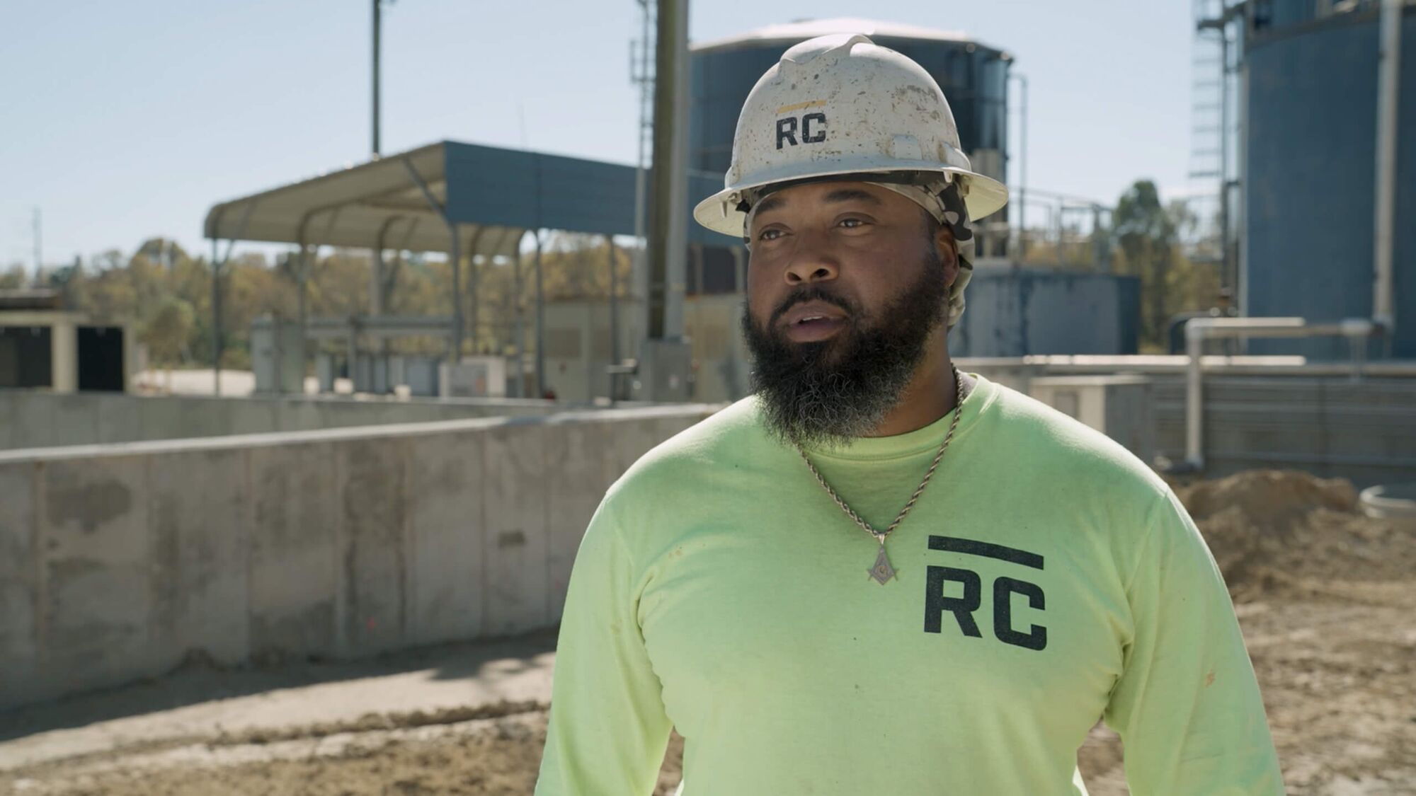 Still image of a construction worker on the jobsite in a white hard hat and a neon green tshirt. 