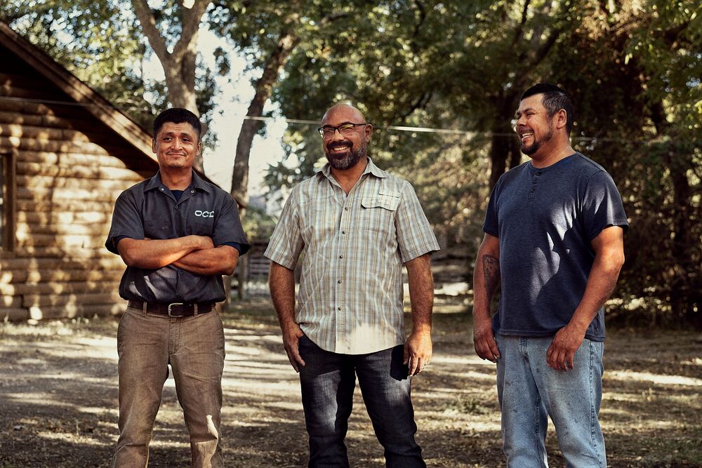 James Oglesby stands proudly in front of a log cabin with two fellow tradespeople