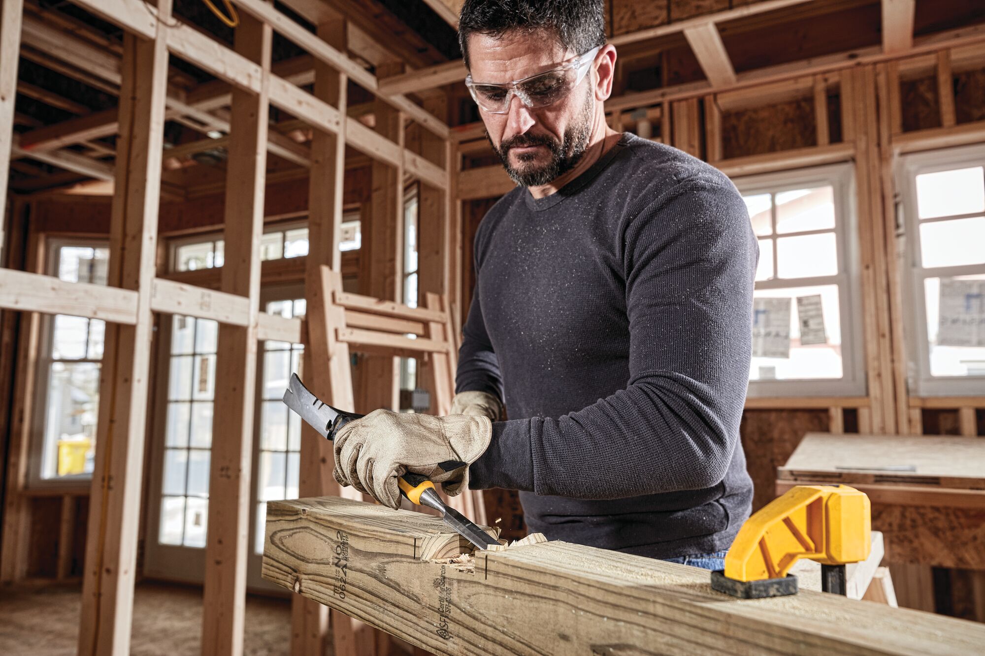 One and a half inch Wood Chisel being struck with hammer by worker to scrape wooden log surface at worksite.