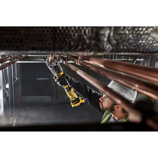 DEWALT Compact Press Tool pressing copper pipe overhead in a mechanical room.