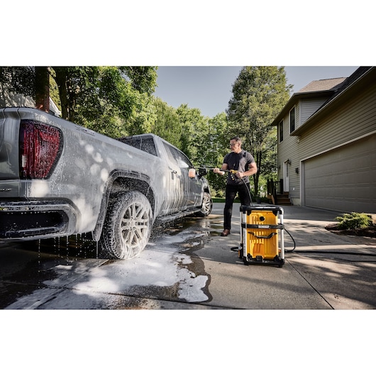 DEWALT 15 Amp Electric Cold Water Pressure Washer being used by a man to clean a truck in the driveway of a house.