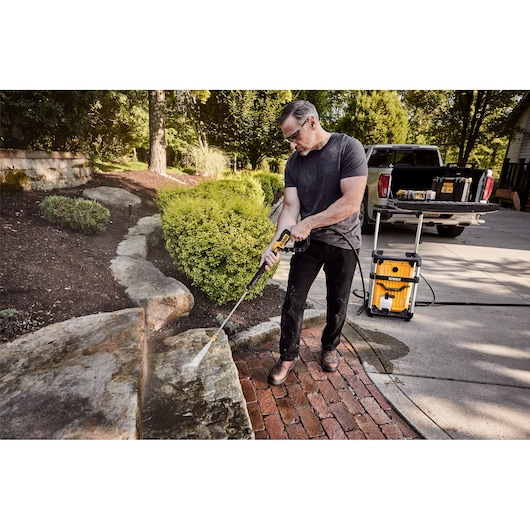 DEWALT 15 Amp Electric Cold Water Pressure Washer being used by a man to clean stone steps in front of a house. 