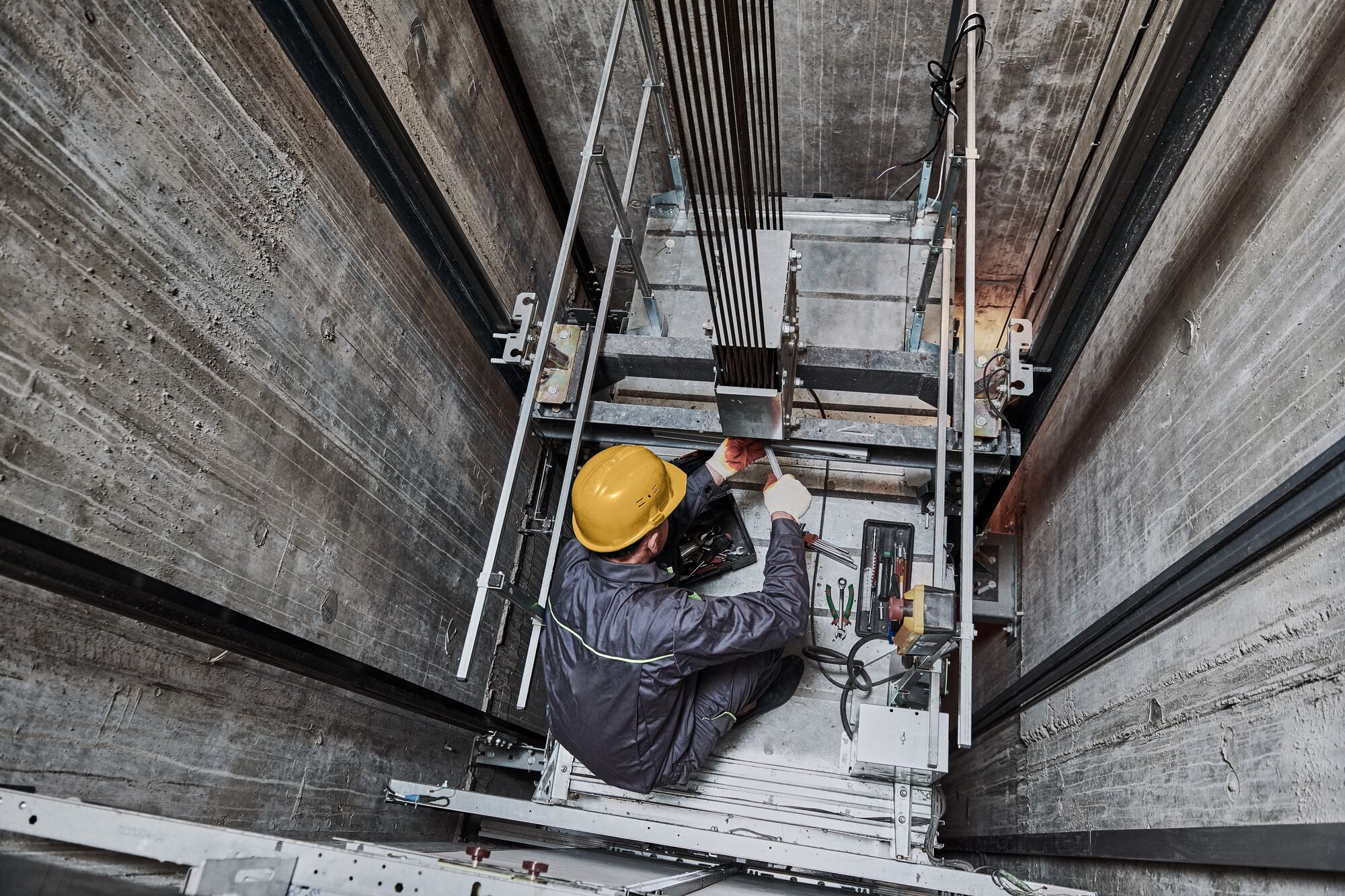 A worker using a wrench on the top of an elevator in a shaft