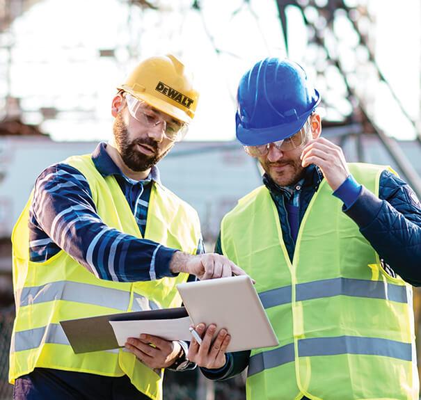 Two workers in helmets looking and pointing at a tablet